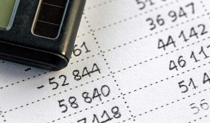 Calculator resting on a financial statement with columns of accounting figures and handwritten-style numbers.