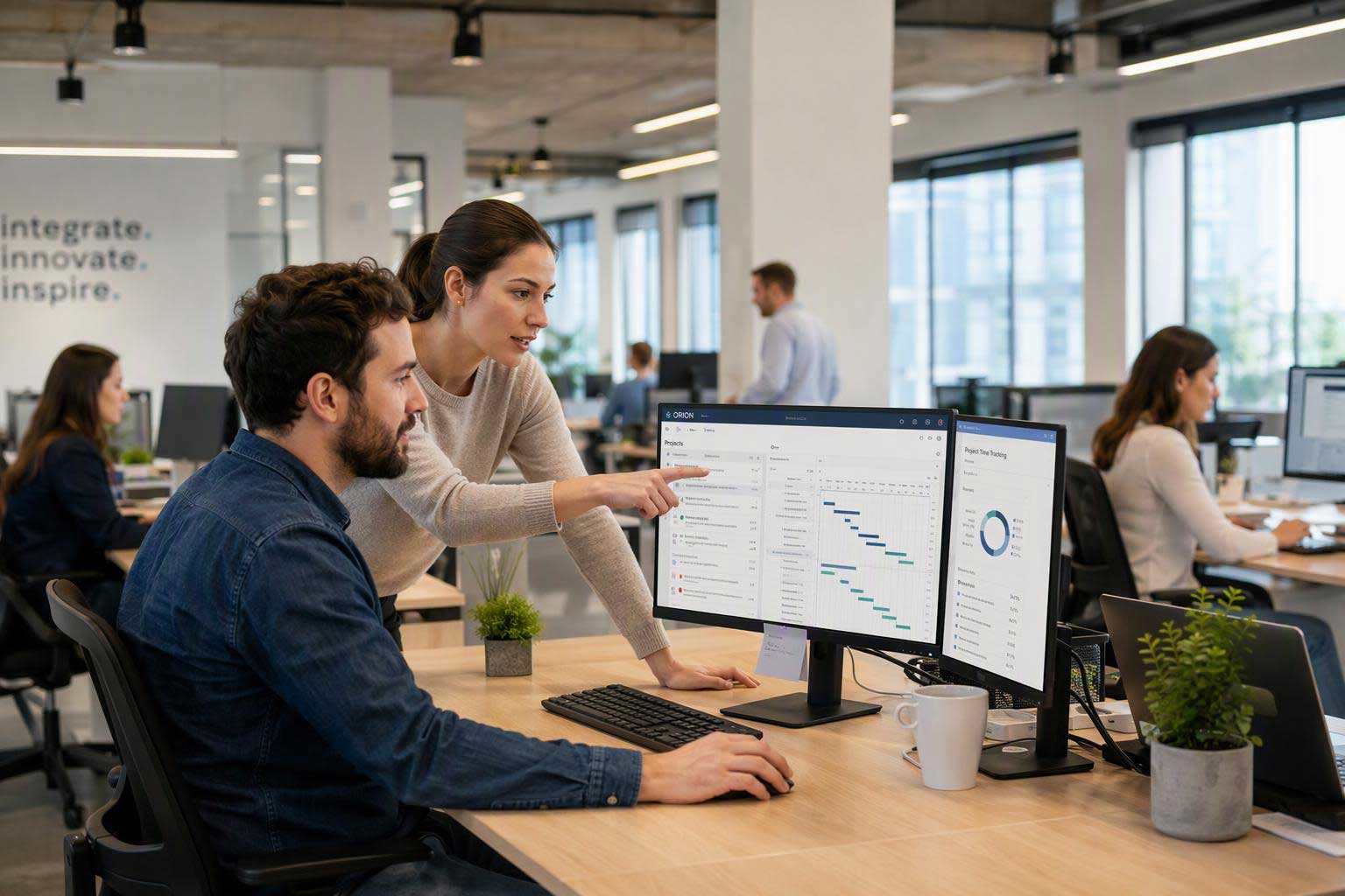 Office team reviewing project management software with task schedules, timelines, and performance data on dual monitors.