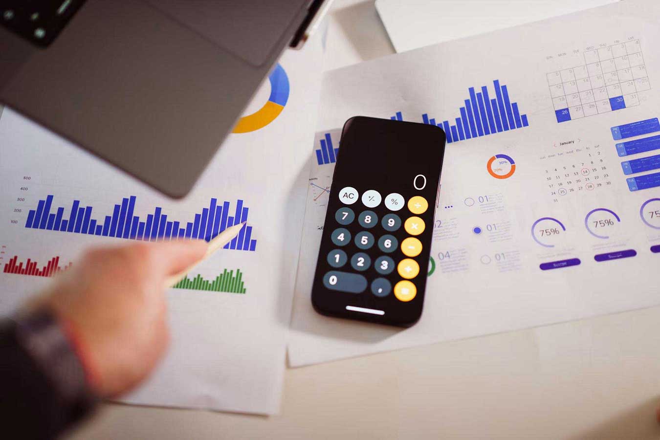 Smartphone calculator resting on printed financial reports with colorful bar charts, graphs, and business performance data.