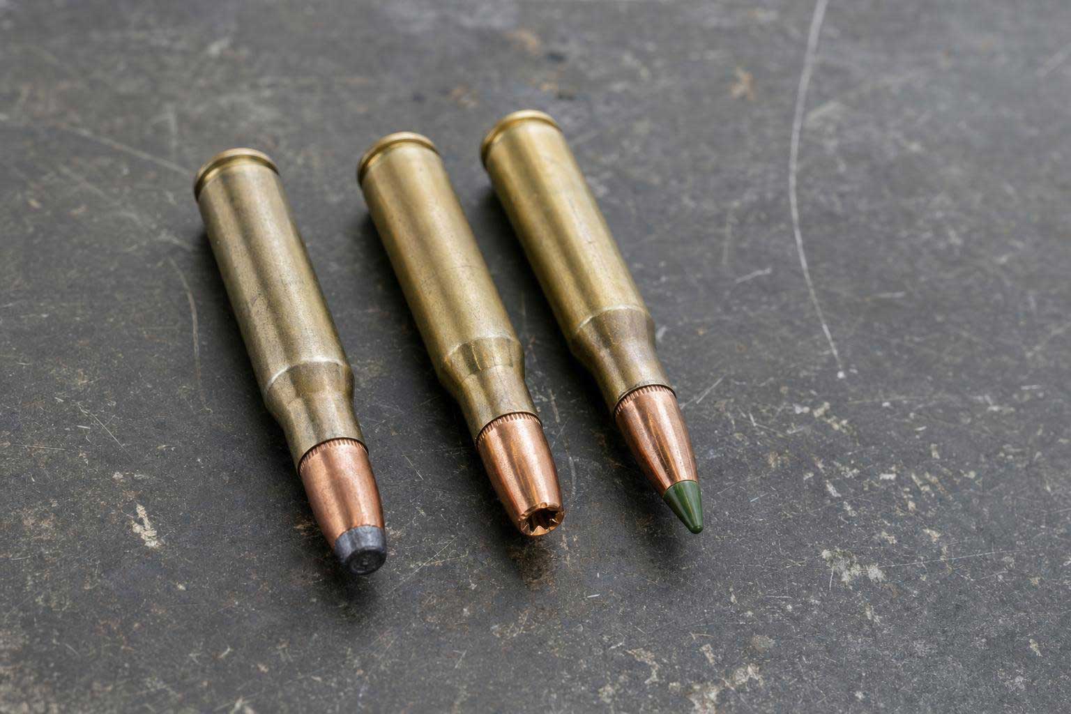 Three rifle cartridges with different bullet styles displayed on a metal workbench.