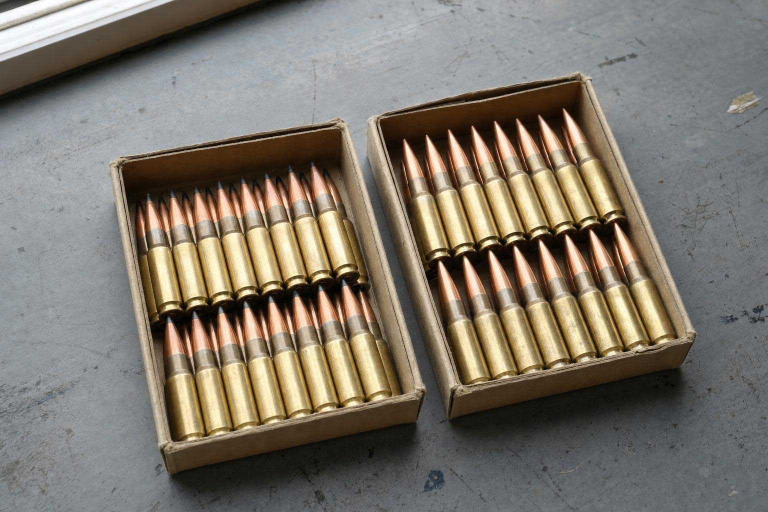 Two open cardboard boxes filled with rifle cartridges featuring pointed copper bullets.