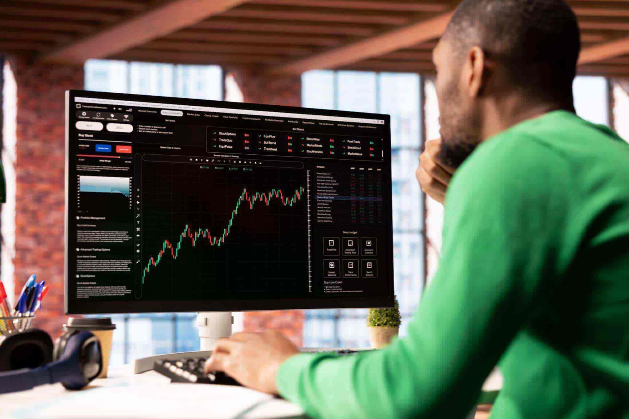A man sitting at a desk looking at a stock chart on a montior.