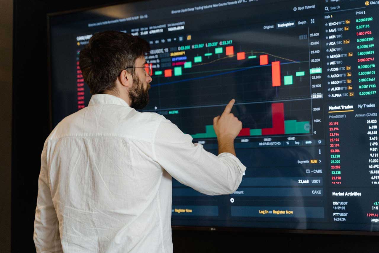 A person standing in front of a large monitor with stock charts on it.